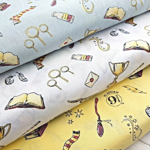 May include: Three fabric panels with a Harry Potter theme. The top panel is light blue with a white background and features images of a book, a wand, a feather, and a scarf. The middle panel is white with a yellow background and features images of a book, a wand, a feather, and a cup. The bottom panel is yellow with a white background and features images of a book, a wand, a feather, a cup, a lightning bolt, and a platform 9 3/4 sign.