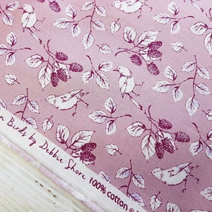 Op de afbeelding: Roze stof met een wit bloemenpatroon met vogels en bessen. De stof heeft de tekst "Garden Birds by Debbie Shore 100% cotton" erop gedrukt.