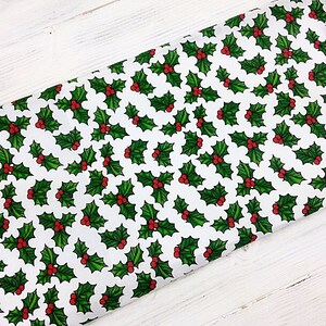 May include: White fabric with a repeating pattern of green holly leaves and red berries.