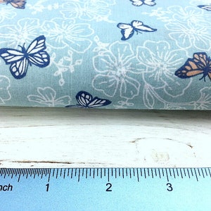 May include: A light blue fabric with a white floral pattern and brown and blue butterflies. The fabric is measured with a ruler showing 4 inches.