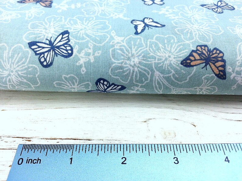 May include: A light blue fabric with a white floral pattern and brown and blue butterflies. The fabric is measured with a ruler showing 4 inches.