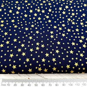 May include: Navy blue fabric with a repeating pattern of gold stars. The stars vary in size and are scattered across the dark blue background. A ruler with millimeter markings is at the bottom of the image.