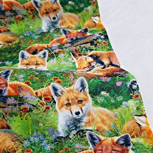 May include: A repeating pattern of red foxes in a green field with orange, blue, and white flowers. The foxes are in various poses, some are sleeping, some are sitting, and some are looking at the viewer.