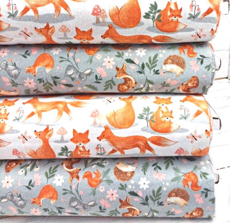May include: Four rolls of fabric with a repeating pattern of foxes, mushrooms, and flowers. The fabric is in shades of blue, white, and orange.