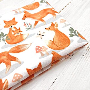 May include: White fabric with a repeating pattern of orange foxes and mushrooms. The foxes are depicted in various poses, including a mother fox carrying a baby fox.