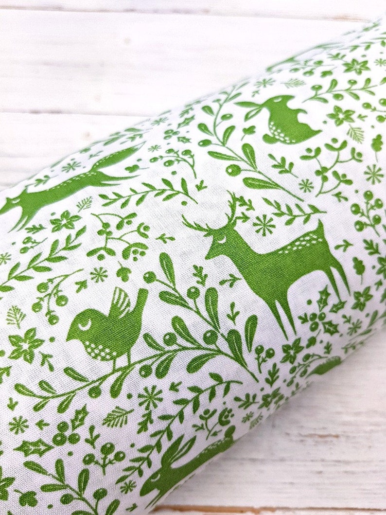 K&ouml;nnte beinhalten: Gr&uuml;ner Stoff mit wei&szlig;em Hintergrund und einem sich wiederholenden Muster aus stilisierten Hirschen, V&ouml;geln, Kaninchen und floralen Elementen.