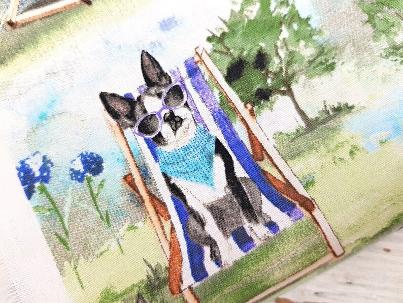 May include: A fabric with a watercolor illustration of a dog relaxing in a beach chair. The dog wears sunglasses and a blue bandana. The background features a green lawn, blue flowers, and trees.