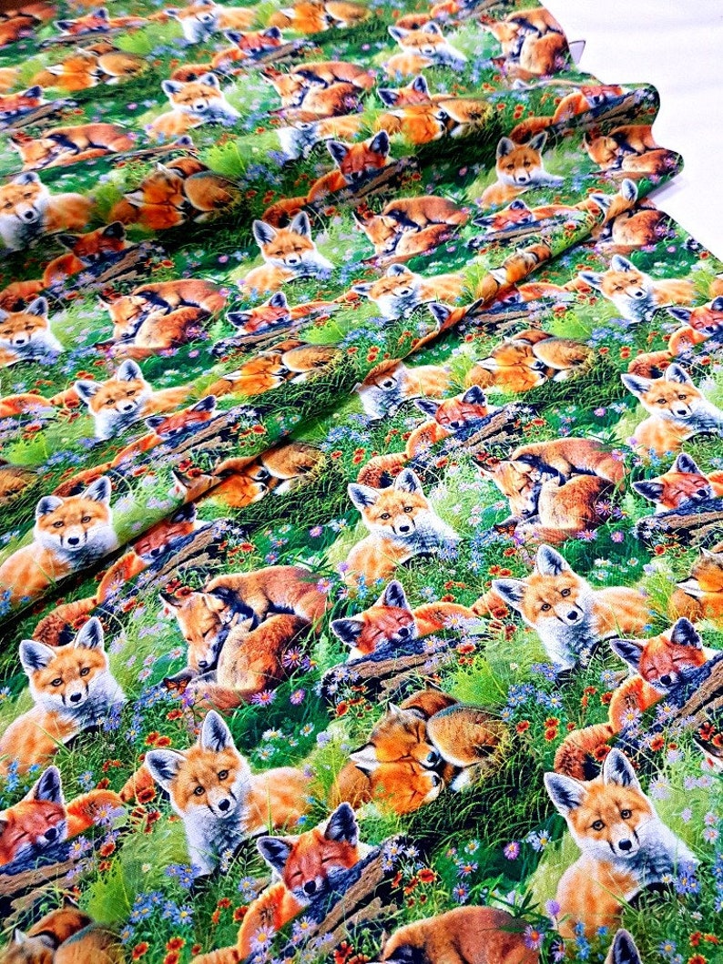 May include: A green fabric with a repeating pattern of red foxes sleeping in a field of green grass and colorful flowers.
