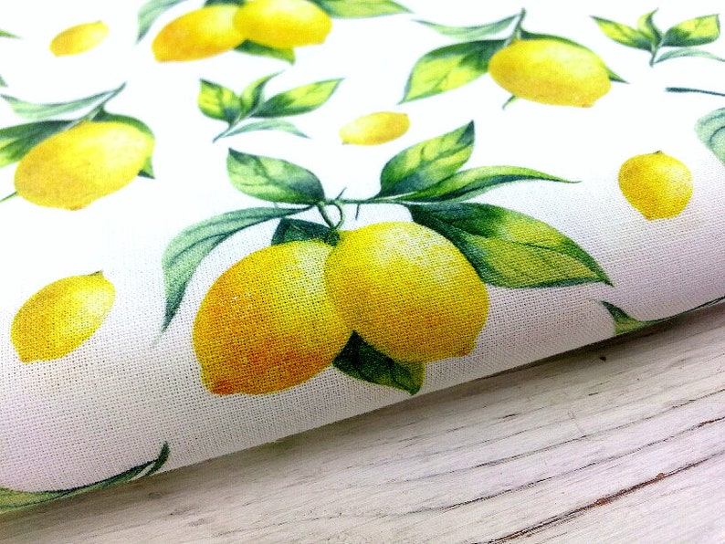 May include: White fabric with a repeating pattern of yellow lemons and green leaves. The lemons are painted in a watercolor style.