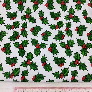 May include: White fabric with a repeating pattern of green holly leaves and red berries. The fabric is labeled "Dressmakers Square" and "DUROEDGE".