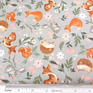 May include: A gray fabric with a repeating pattern of woodland animals and flowers. The animals include foxes, squirrels, deer, rabbits, and hedgehogs. The flowers are pink and white.