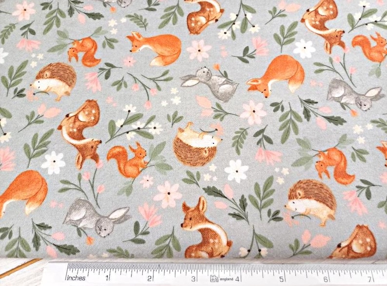 May include: A gray fabric with a repeating pattern of woodland animals and flowers. The animals include foxes, squirrels, deer, rabbits, and hedgehogs. The flowers are pink and white.