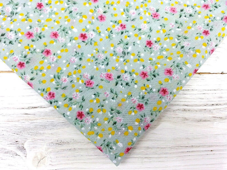 May include: A light green fabric with a small floral print. The print features pink and yellow flowers on a light green background.
