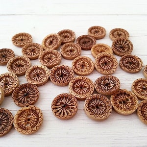 May include: A collection of wooden buttons with a carved floral design. The buttons are a light brown colour and have two holes.