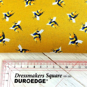 May include: Yellow fabric with a repeating pattern of black and yellow bumblebees. A ruler with the text "Dressmakers Square DUR-O-EDGE KR-360" is in the bottom of the image.