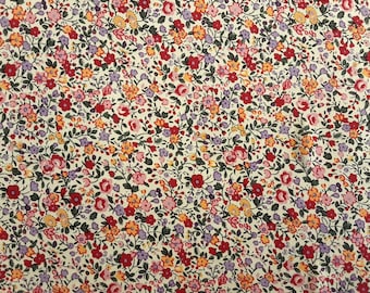 Pode incluir: Um tecido branco com uma estampa floral em pequena escala. A estampa apresenta flores vermelhas, rosas, amarelas e roxas sobre um fundo branco.