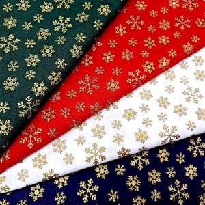 May include: Four folded pieces of fabric featuring a repeating pattern of metallic gold snowflakes. The fabric colors include dark green, bright red, white, and navy blue, each displaying a consistent gold snowflake print design.