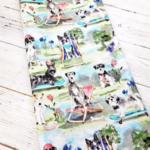 May include: A fabric featuring a repeating pattern of dogs in a park setting. The dogs are depicted in various poses, some on skateboards, others in beach chairs, and some wearing accessories. The color palette includes blues, greens, and pinks.
