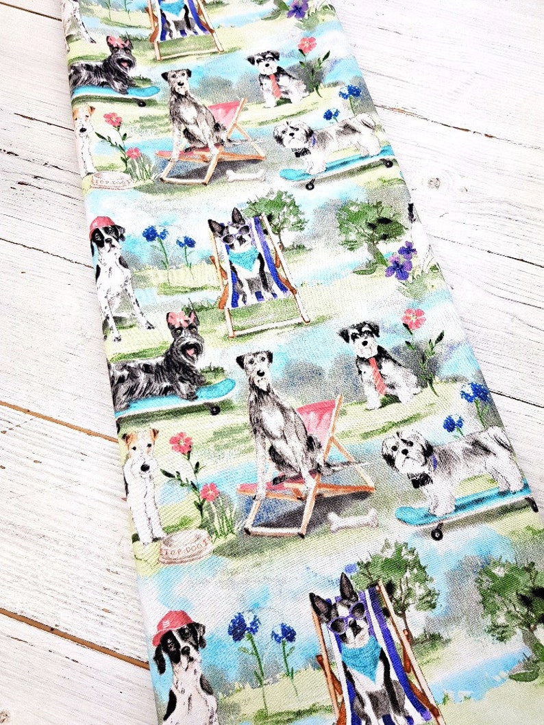 May include: A fabric featuring a repeating pattern of dogs in a park setting. The dogs are depicted in various poses, some on skateboards, others in beach chairs, and some wearing accessories. The color palette includes blues, greens, and pinks.