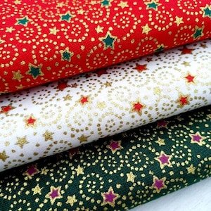 May include: Three folded pieces of fabric stacked vertically. The top piece is red with gold glitter swirls and green stars. The middle piece is white with gold glitter swirls and red stars. The bottom piece is dark green with gold glitter swirls and purple stars.