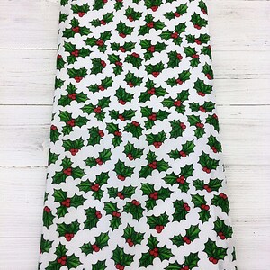 May include: White fabric with a repeating pattern of green holly leaves with red berries.