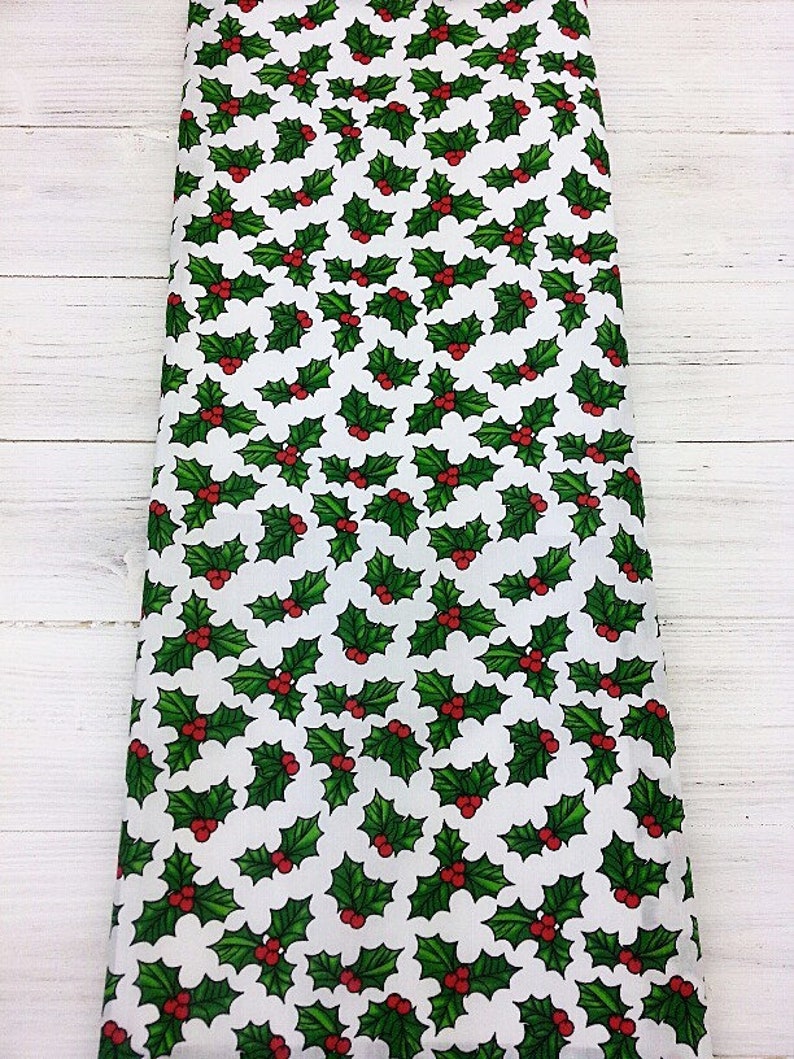 May include: White fabric with a repeating pattern of green holly leaves with red berries.
