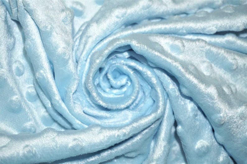 Op de afbeelding: Close-up van een lichtblauwe stof met een textuur van bubbels. De stof is zacht en pluche en perfect voor het maken van dekens, kussens of andere woonaccessoires.