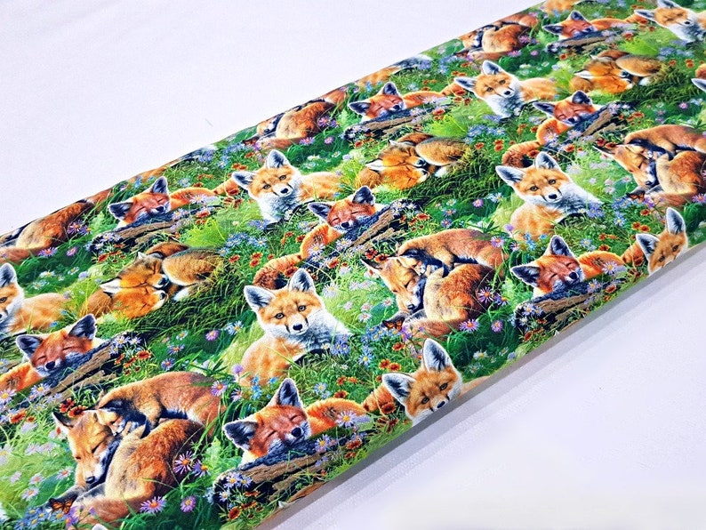 May include: A colorful fabric with a repeating pattern of sleeping foxes in a green grassy field with flowers. The foxes are brown and orange with white accents.