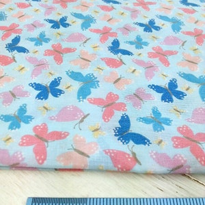 May include: A light blue fabric with a repeating pattern of pink, blue, and yellow butterflies. A ruler is included to show the scale of the fabric.