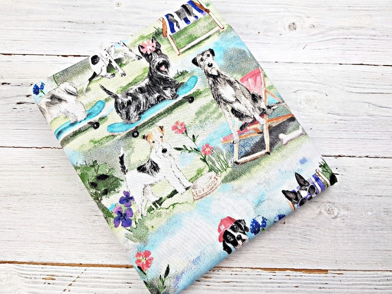 May include: A light blue and white fabric with a colorful print of dogs enjoying leisure activities. The dogs are depicted skateboarding, relaxing in beach chairs, and playing in a garden setting with flowers.