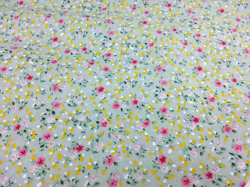 May include: A light green fabric with a small floral print. The print features pink and yellow flowers on a light green background.