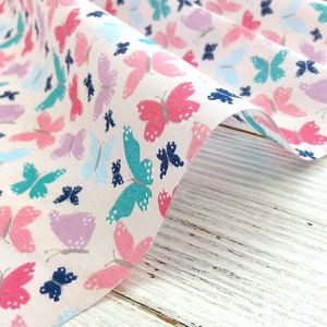 May include: White fabric with a repeating pattern of colorful butterflies. The butterflies are in shades of pink, blue, teal, and purple.