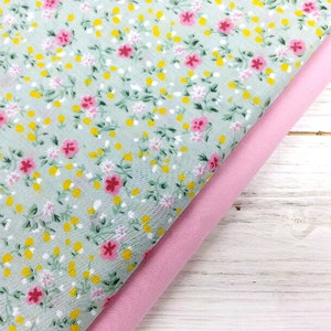 May include: Two pieces of fabric, one with a light green background and a small floral pattern in pink and yellow, and the other a solid pink fabric.
