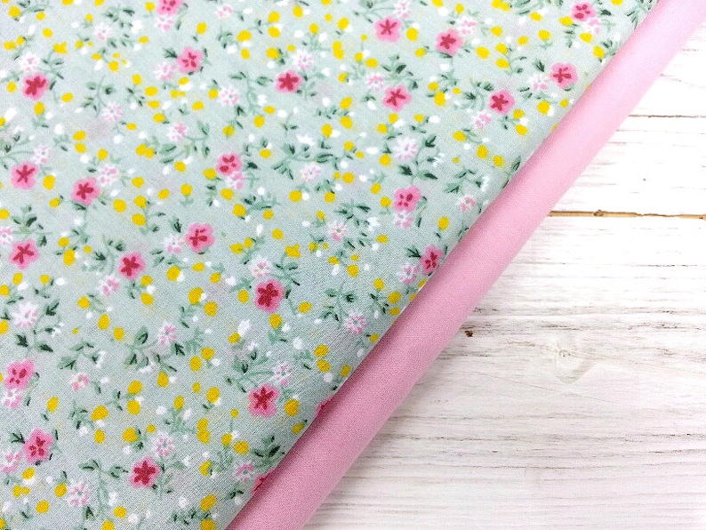 May include: Two pieces of fabric, one with a light green background and a small floral pattern in pink and yellow, and the other a solid pink fabric.