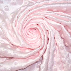 Op de afbeelding: Een close-up van een zachte, roze stof met een textuur, gestippeld patroon. De stof is gevouwen en gekreukt, waardoor een wervelend effect ontstaat.