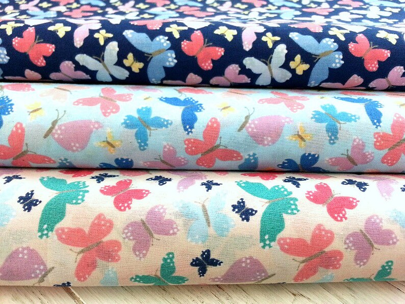 May include: Three fabric swatches with a butterfly print. The top swatch is navy blue with white, yellow, and pink butterflies. The middle swatch is light blue with pink, white, and yellow butterflies. The bottom swatch is cream with pink, purple, and teal butterflies.