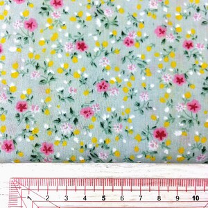 May include: A close-up of a light green fabric with a small floral print. The fabric has tiny yellow and pink flowers with green leaves. A ruler is visible at the bottom of the image, showing the fabric is 10 inches wide.
