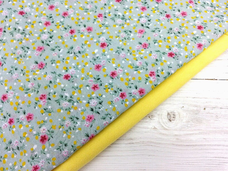 May include: A close-up of two fabric swatches. The top swatch is a light gray fabric with a small pink and yellow floral print. The bottom swatch is a solid yellow fabric.