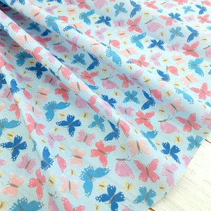 May include: A light blue fabric with a repeating pattern of pink, blue, and white butterflies. The butterflies are scattered randomly across the fabric.