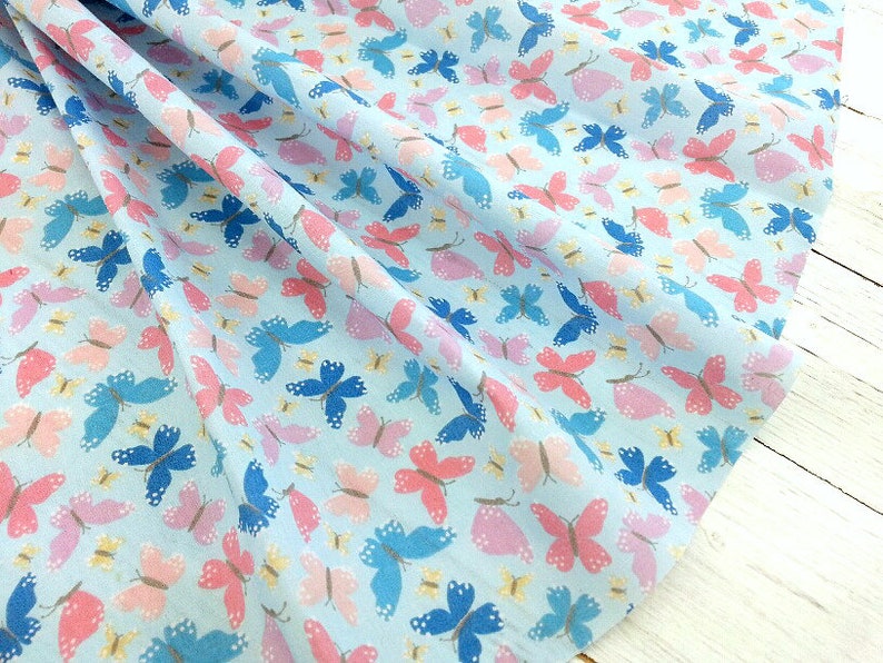 May include: A light blue fabric with a repeating pattern of pink, blue, and white butterflies. The butterflies are scattered randomly across the fabric.