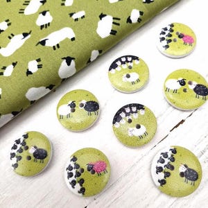 May include: A set of eight wooden buttons with a green background and a black and white sheep design. The buttons feature a flock of sheep with a single black sheep in the middle.