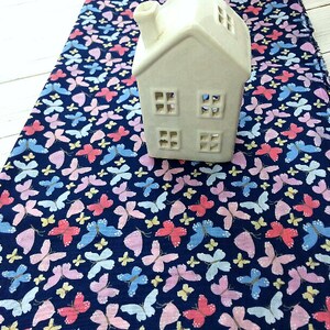 May include: A navy blue fabric with a repeating pattern of pink, blue, and yellow butterflies. A white ceramic house sits on top of the fabric.