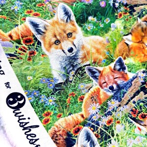 May include: A colorful fabric with a repeating pattern of foxes in a field of flowers. The foxes are orange, white, and brown, and the flowers are pink, purple, yellow, and red. The fabric has a white border with the text "Brushes Fabric" printed on it.