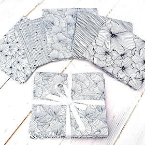 Peut inclure: Un ensemble de six carrés de tissu noir et blanc avec différents motifs géométriques et floraux. Les carrés de tissu sont disposés en cercle sur une surface en bois blanc.