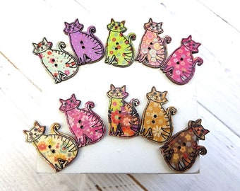 May include: Nine colorful wooden cat buttons with floral patterns. The buttons are approximately 2 inches in diameter and have two holes for sewing.