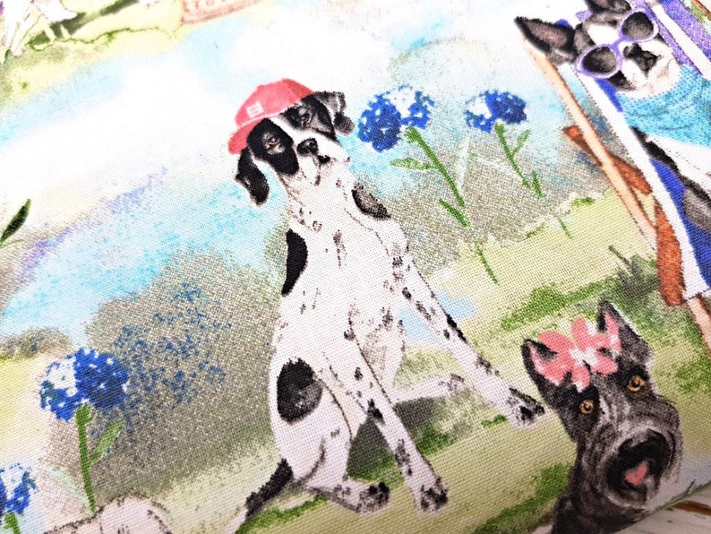 May include: Fabric featuring a whimsical illustration of dogs in a park setting. A Dalmatian wearing a red cap is the focal point, surrounded by other dogs, blue flowers, and a light blue and green background.