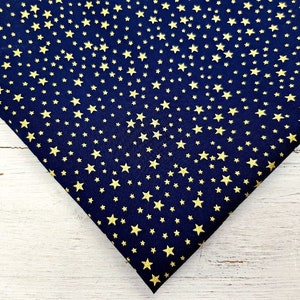 May include: Navy blue fabric with a repeating pattern of gold stars. The stars vary in size and are evenly distributed across the fabric. The fabric is folded, showing the texture and color contrast.