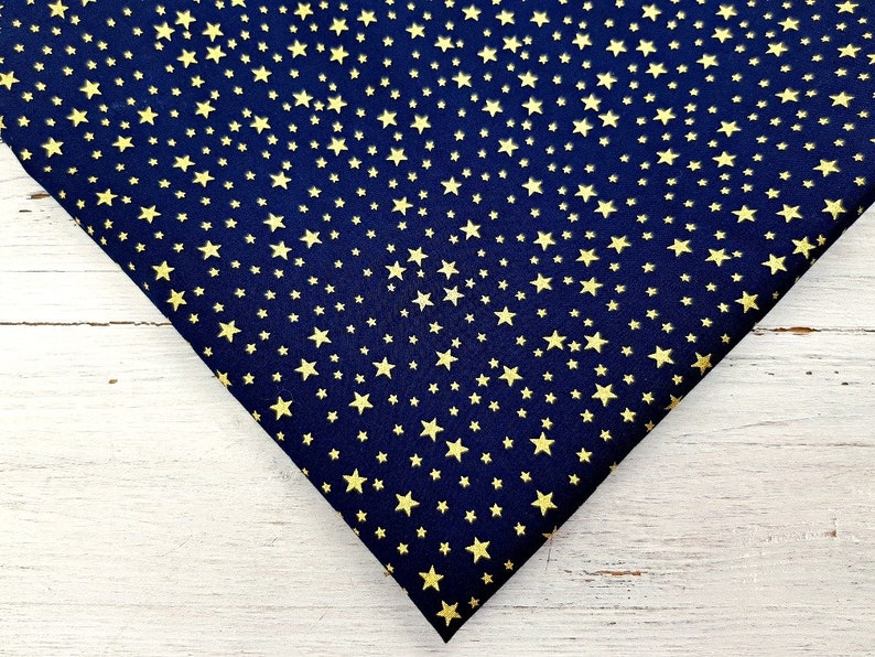 May include: Navy blue fabric with a repeating pattern of gold stars. The stars vary in size and are evenly distributed across the fabric. The fabric is folded, showing the texture and color contrast.