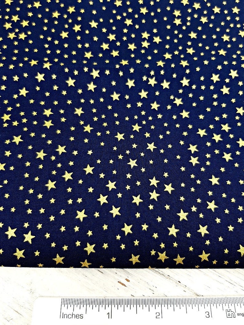 May include: Dark navy blue fabric with a repeating pattern of gold stars. The stars vary in size and are scattered across the material. A ruler with inch measurements is at the bottom of the image.