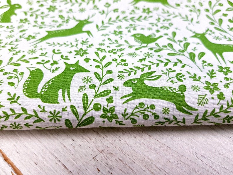 K&ouml;nnte beinhalten: Gr&uuml;ner Stoff mit wei&szlig;em Hintergrund und einem sich wiederholenden Muster aus F&uuml;chsen, Rehen, Kaninchen, V&ouml;geln und Blumenmotiven.